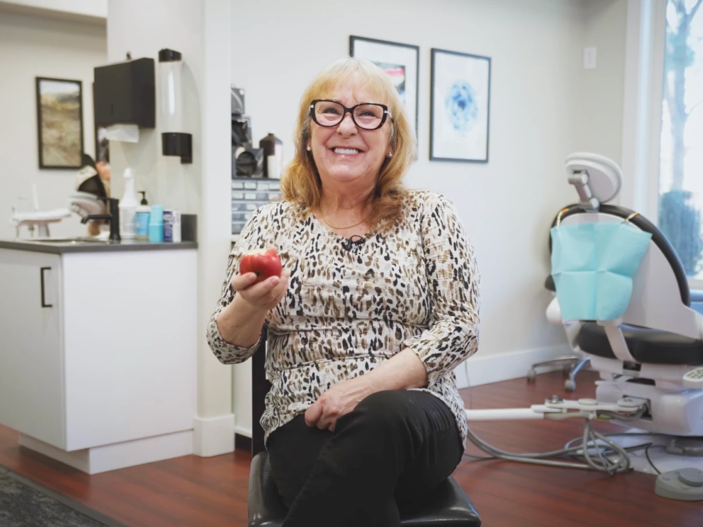 A woman eating after implant surgery and smiling after biting into an apple.